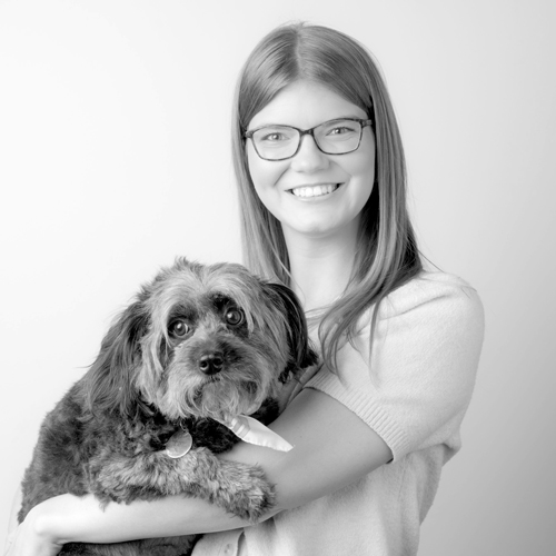 Smiling woman with glasses holding a fluffy small dog in her arms.