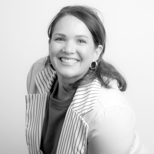 Smiling woman with hoop earrings wearing a striped blazer and dark top, looking at the camera.