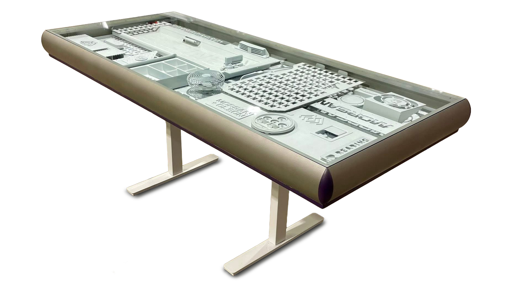 Long glass-topped display table showing white mechanical components inside, supported by two white stands.