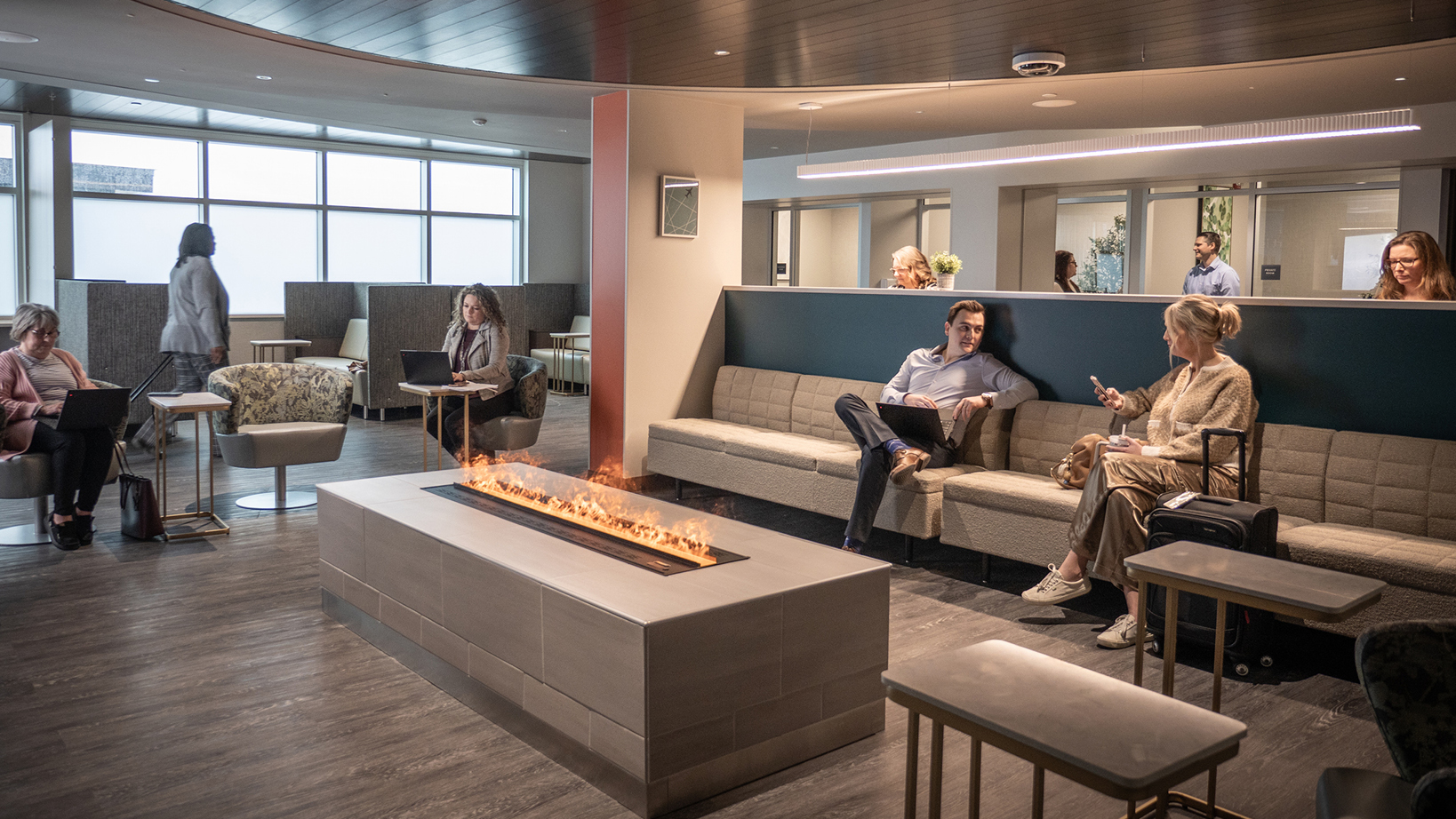 Modern office lounge with a rectangular gas fireplace and people using laptops on couches and chairs nearby.