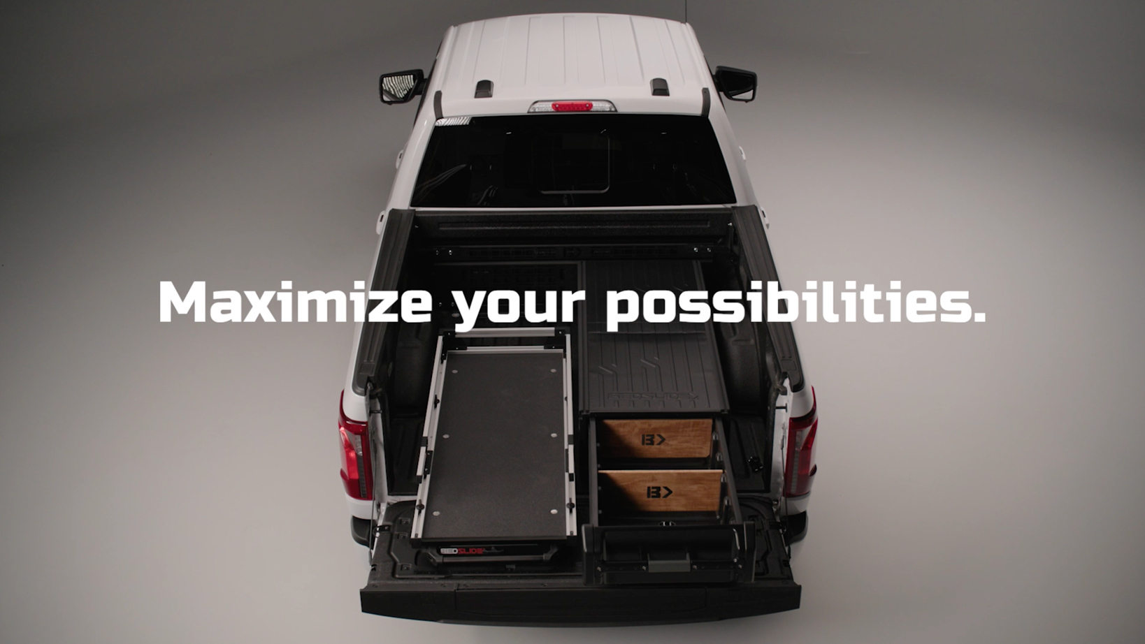 Top-down view of a white pickup with its bed open, showing a modular drawer system and wooden crates beneath a bold slogan: Maximize your possibilities.