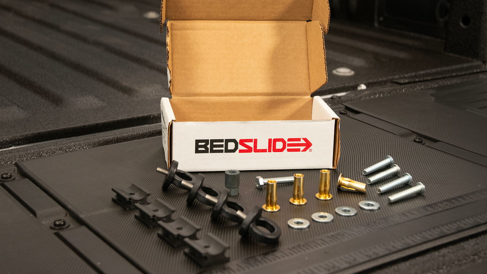 Open BedSlide box in a pickup bed with assorted mounting hardware (bolts, washers, nuts) laid out for installation.