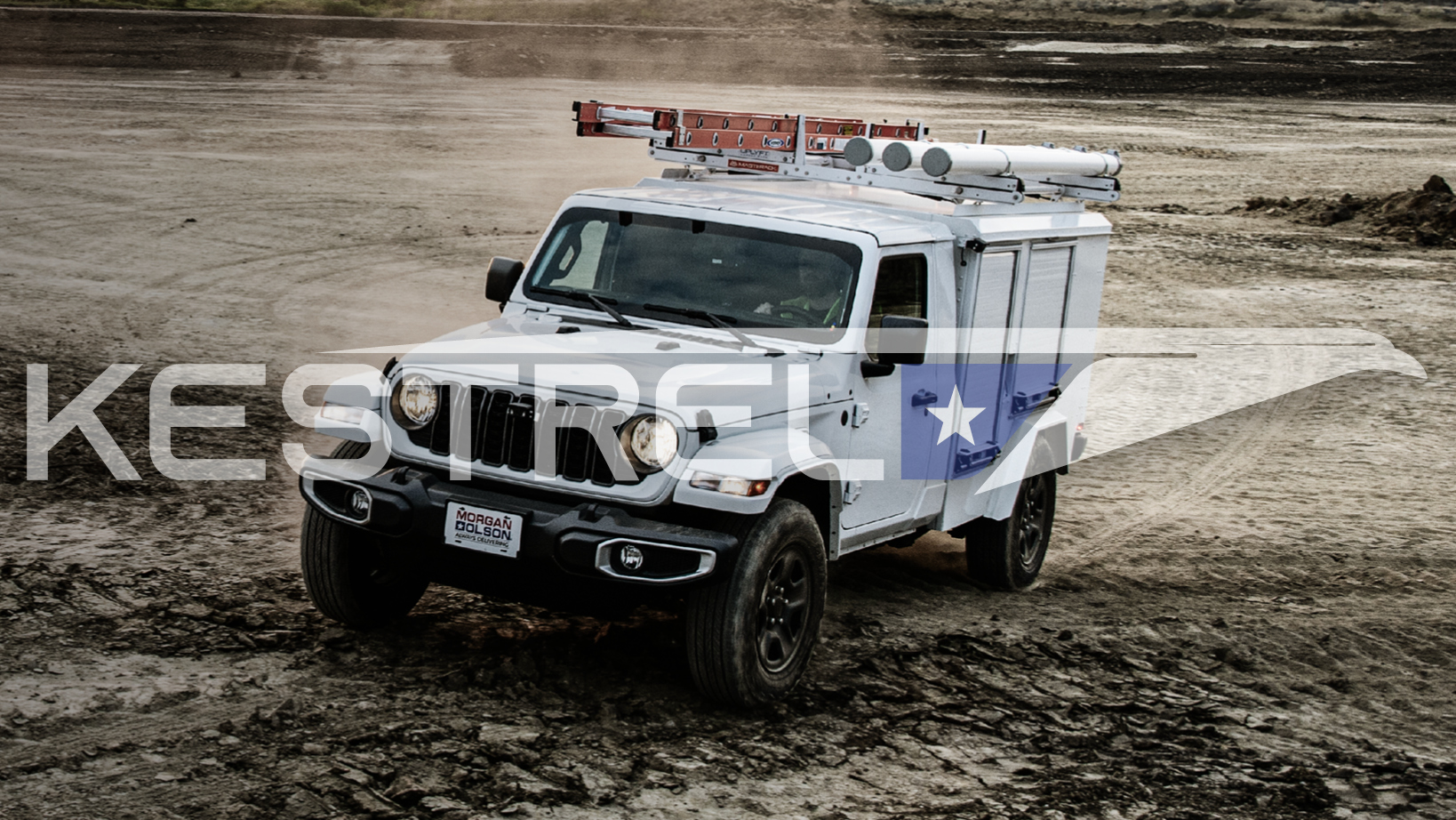 White utility truck with ladder rack driving on a muddy construction site.