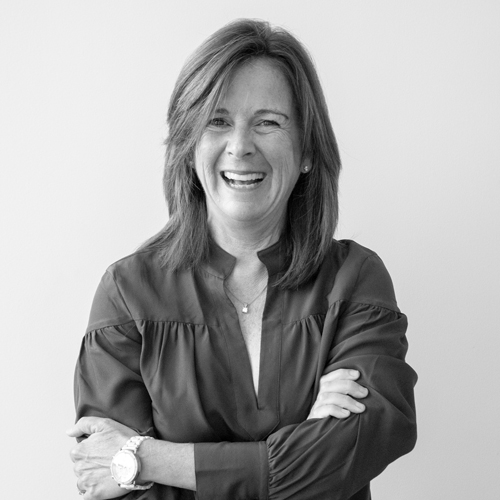 Smiling woman with arms crossed, wearing a dark blouse, posing against a light background.