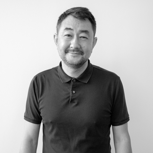 Portrait of a man wearing a dark polo shirt, smiling, standing against a plain light background (head and shoulders).