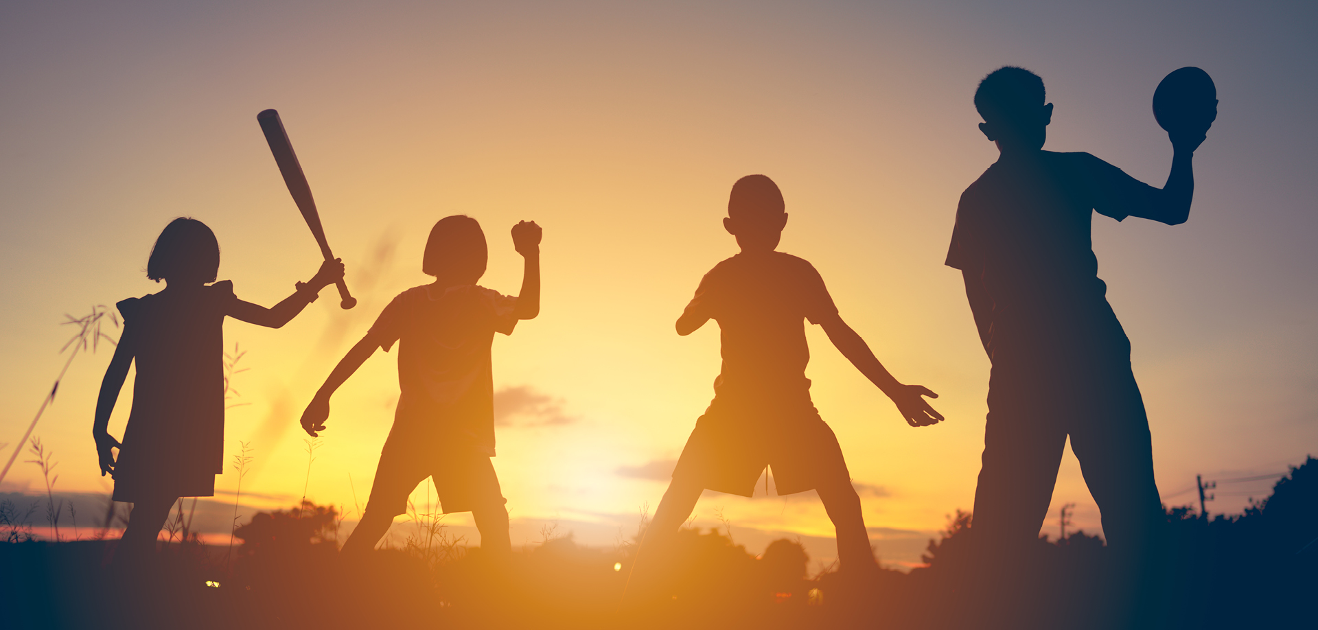 Silhouettes of four children playing baseball at sunset; one holds a bat while others cheer or pose ready to play.