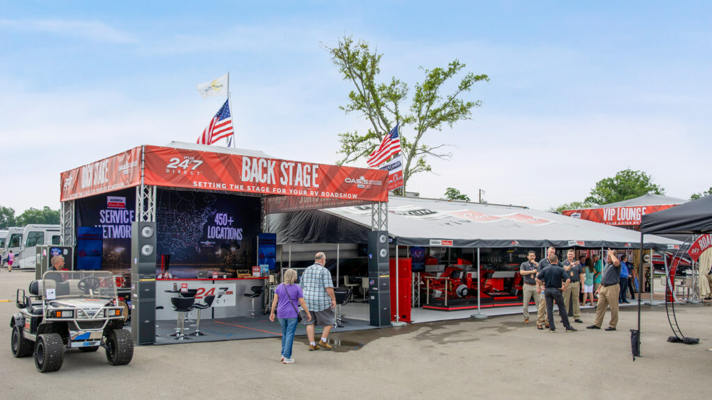 Event booth with a red stage banner reading 'BACK STAGE' and people gathered nearby at an RV roadshow site.