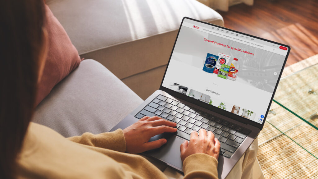 Person sitting on a beige sofa and using a laptop to browse a cleaning products webpage on the screen.